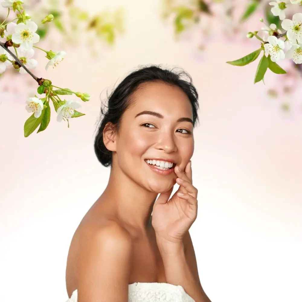 Naturalna kobieta w ręczniku, dotyka twarzy, nad nią gałązki kwitnącej wiśni..