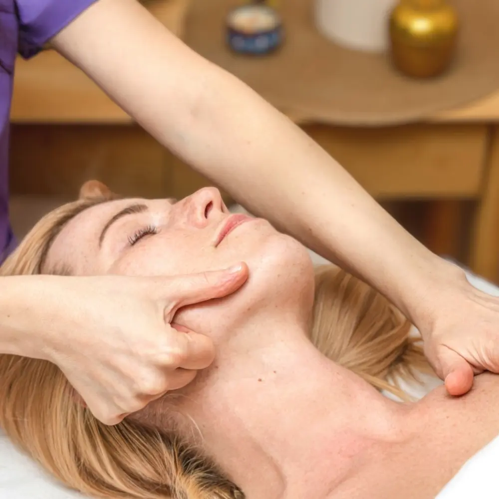 Primo piano di una donna naturale che appoggia le mani sulle guance, in un gesto di rilassamento e cura del viso.