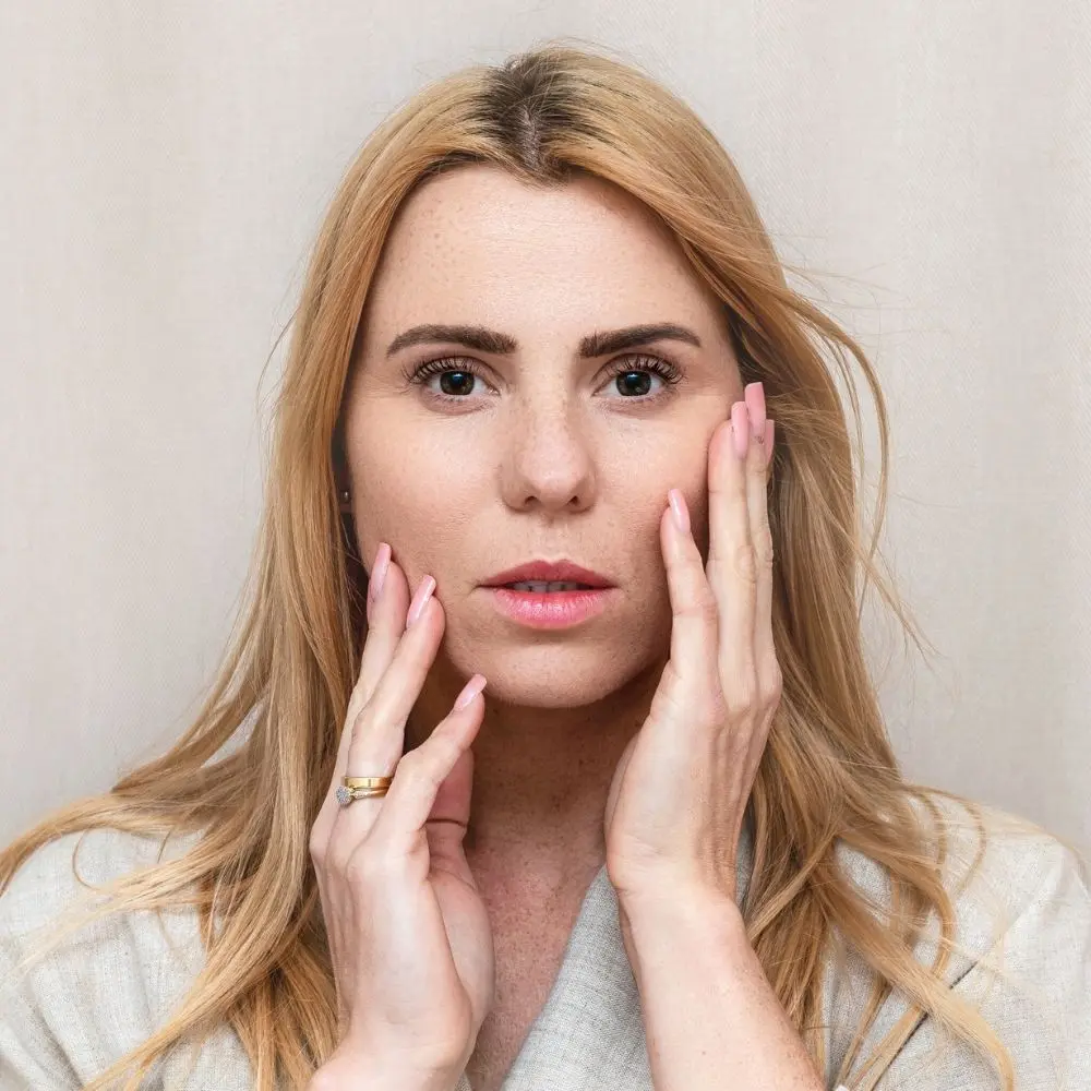 Primo piano di una donna naturale che appoggia le mani sulle guance, in un gesto di rilassamento e cura del viso.