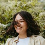 Uśmiechnięta dziewczyna w czarnych włosach do ramion, na tle zieleni.