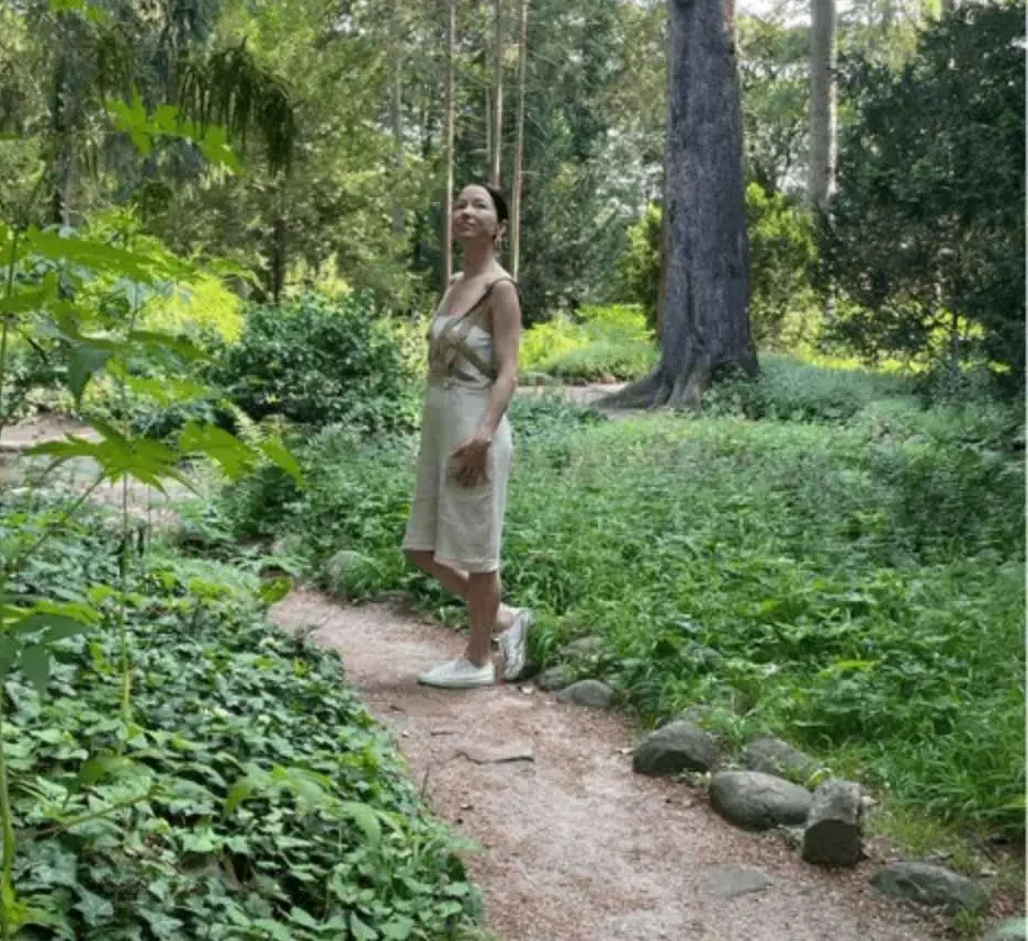 Kobieta patrząca w górę, na tle zieleni parku Oliwskiego w Gdańsku.